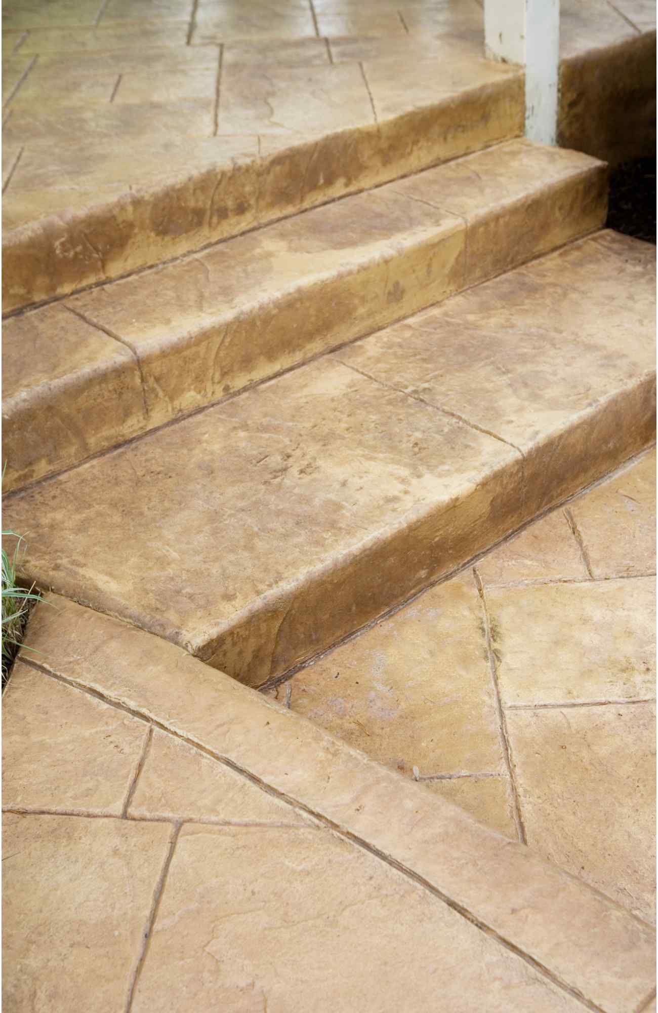 A close-up view of a concrete patio area with two steps leading up to a second level in Paradise Valley. The surface has a textured, stamped pattern resembling natural stone. The edges of the steps are clean and sharp, with the ground slightly sloped for drainage, showcasing work by a licensed concrete contractor.