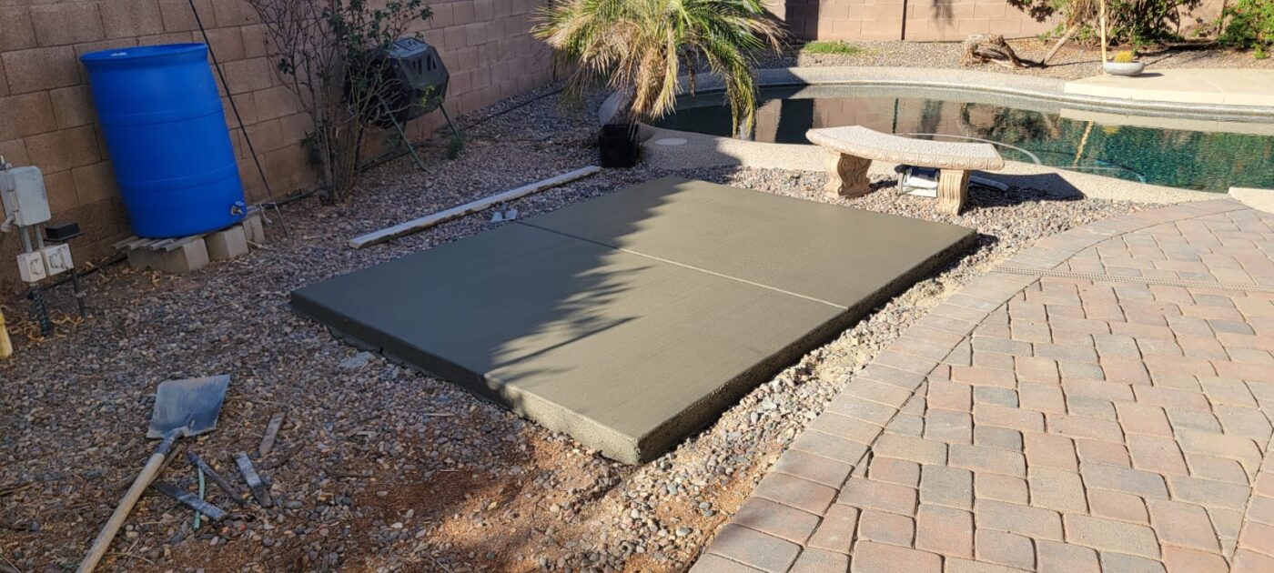 A concrete contractor in Gilbert AZ operates a pump, discharging wet concrete onto the construction site and filling a steel rebar framework. Workers in the background attend to leveling and smoothing the freshly poured concrete. The scene shows a work in progress on a structural slab. Free quotes available!